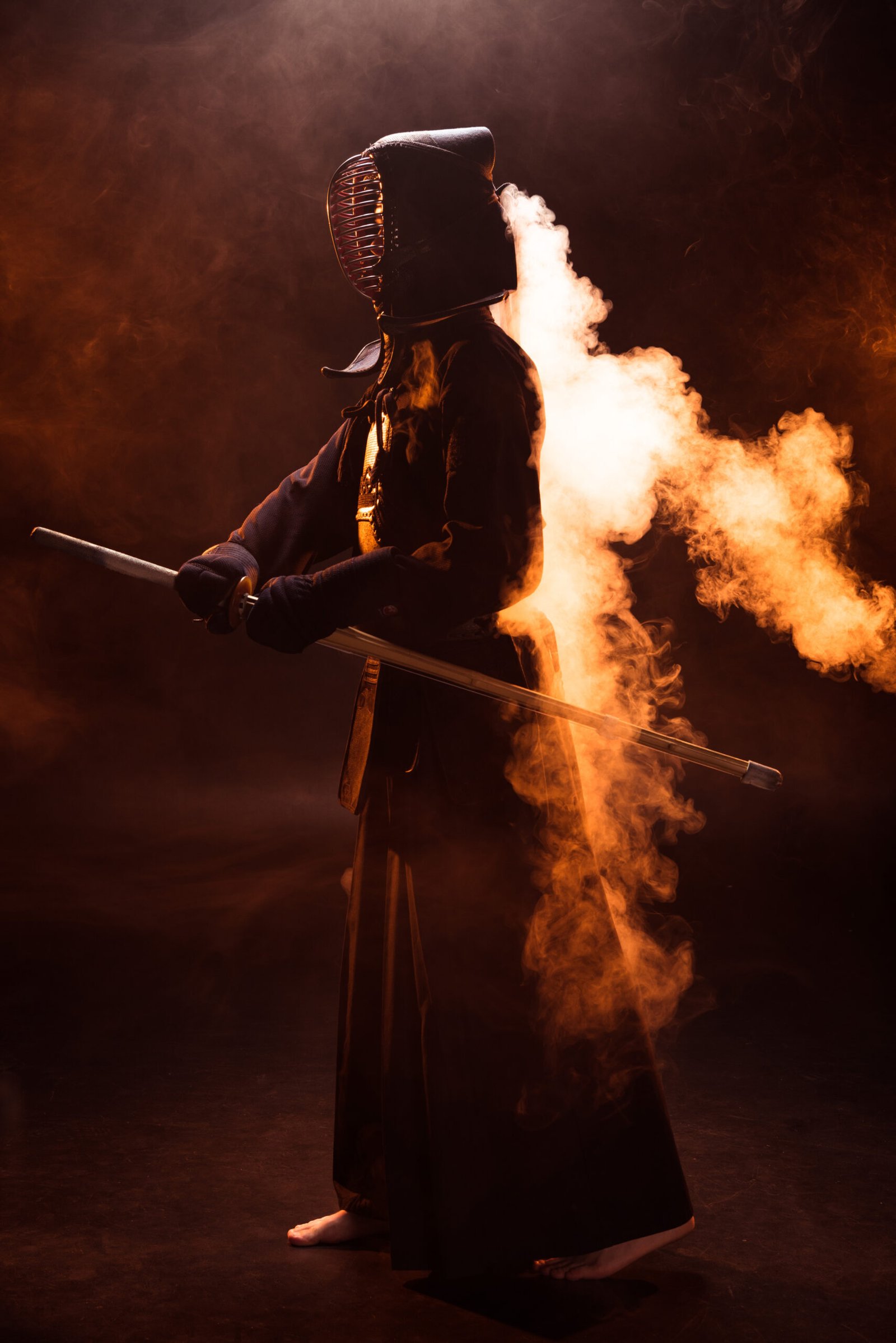 full length view of kendo fighter in armor holding bamboo sword in smoke